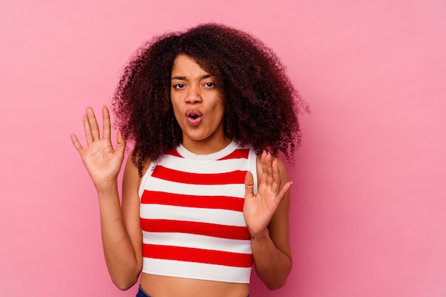 Jeune femme afro-américaine isolée sur fond rose rejetant quelqu'un montrant un geste de dégoût.