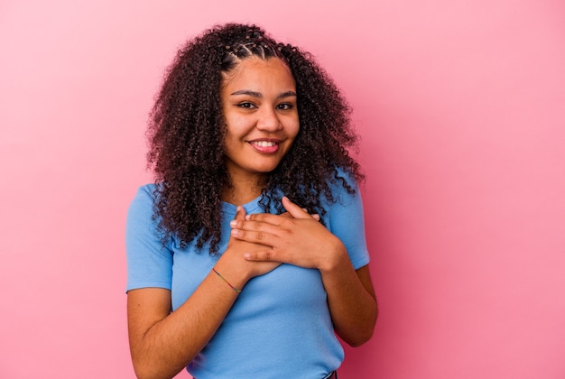 Jeune femme afro-américaine isolée sur fond rose en riant en gardant les mains sur le cœur, concept de bonheur.