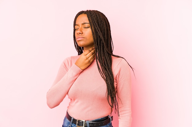 Jeune femme afro-américaine isolée sur fond rose souffre de douleurs dans la gorge en raison d'un virus ou d'une infection.