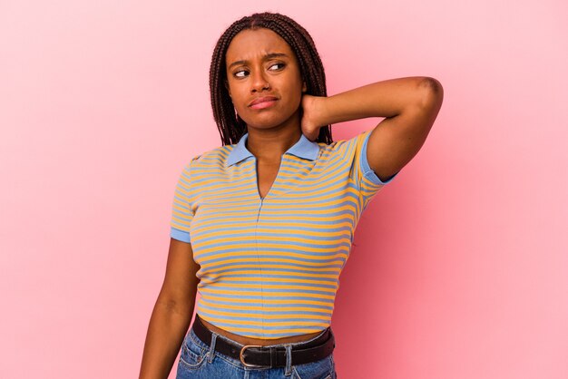 Jeune femme afro-américaine isolée sur fond rose touchant l'arrière de la tête, pensant et faisant un choix.