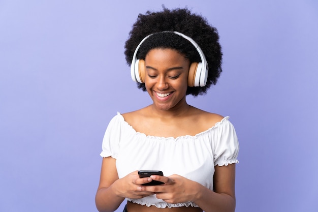 Jeune femme afro-américaine isolée sur fond violet, écouter de la musique et à la recherche de mobile