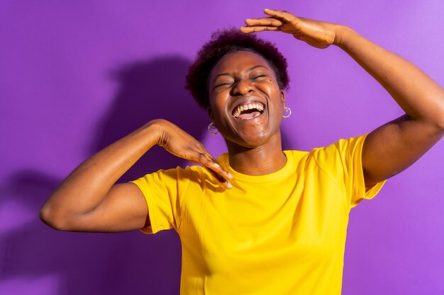 Jeune femme afro-américaine isolée sur fond violet souriant et dansant en studio