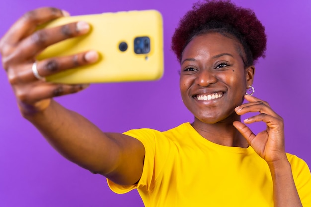 Jeune femme afro-américaine isolée sur fond violet souriant et faisant un tournage en studio selfie