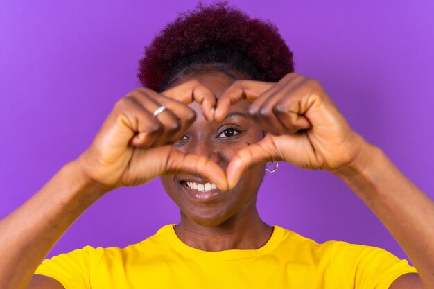 Jeune femme afro-américaine isolée sur fond violet souriant et tournage en studio de geste cardiaque