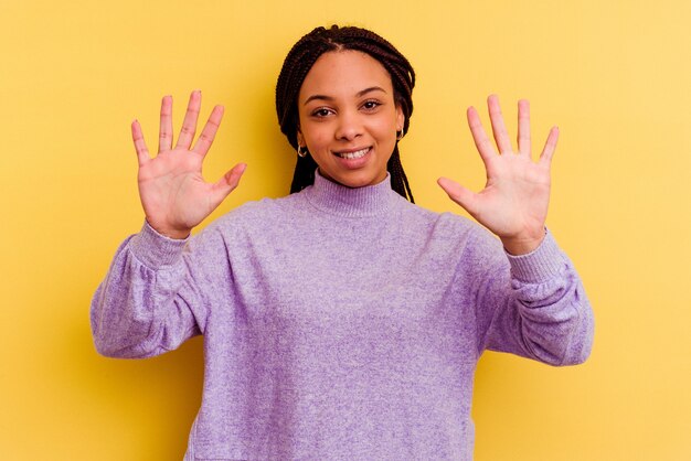 Jeune femme afro-américaine isolée sur jaune montrant le numéro dix avec les mains.