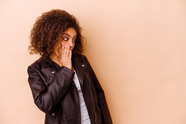 Jeune femme afro-américaine isolée sur un mur beige étant choquée à cause de quelque chose qu'elle a vu.