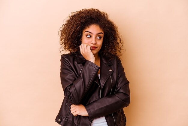 Jeune femme afro-américaine isolée sur un mur beige se mordant les ongles, nerveuse et très anxieuse.