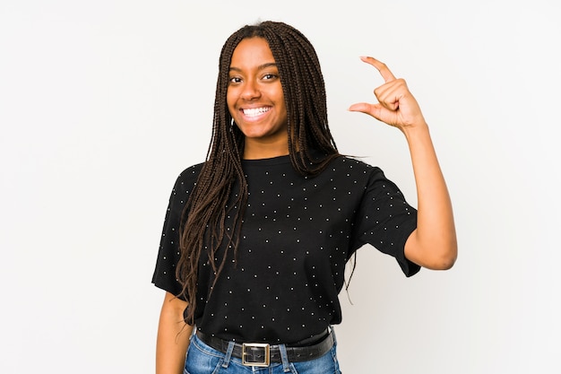 Jeune femme afro-américaine isolée sur mur blanc tenant quelque chose de peu avec les index, souriant et confiant.