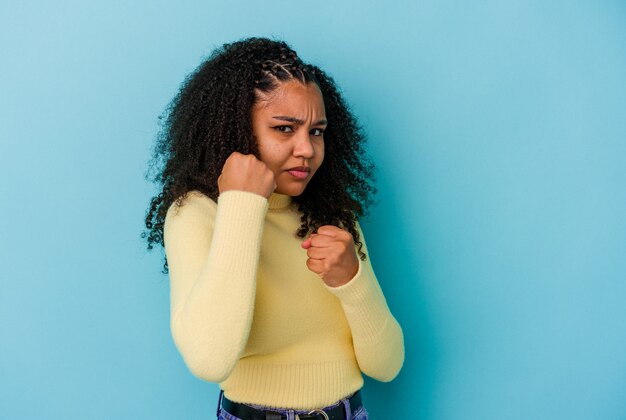 Jeune femme afro-américaine isolée sur le mur bleu jetant un coup de poing, la colère, les combats en raison d'une dispute, la boxe