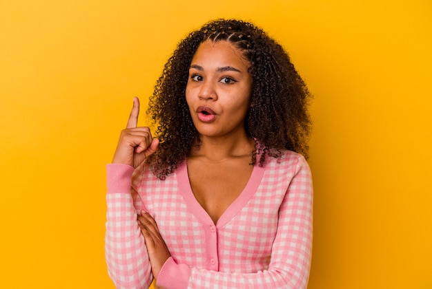 Jeune femme afro-américaine isolée sur un mur jaune ayant une excellente idée, concept de créativité.