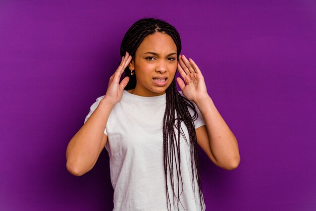 Jeune femme afro-américaine isolée sur un mur jaune couvrant les oreilles avec les doigts, stressée et désespérée par un bruit ambiant.