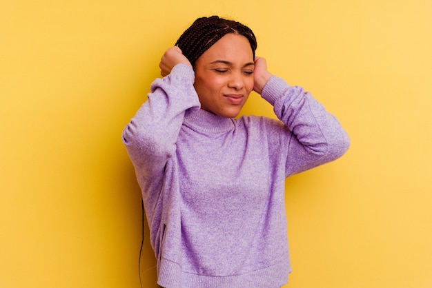 Jeune femme afro-américaine isolée sur un mur jaune couvrant les oreilles avec les mains