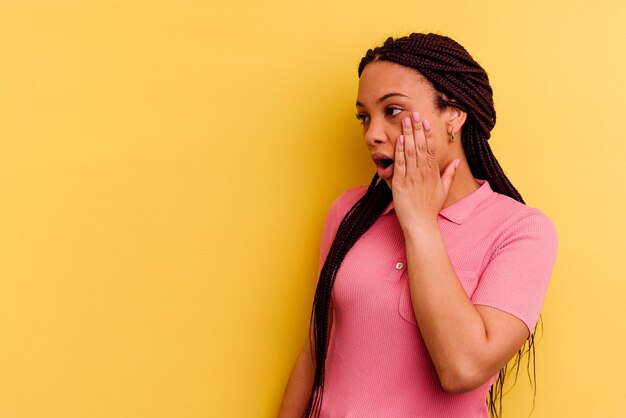 Jeune femme afro-américaine isolée sur un mur jaune étant choquée à cause de quelque chose qu'elle a vu.