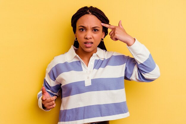Jeune femme afro-américaine isolée sur un mur jaune montrant un geste de déception avec l'index.
