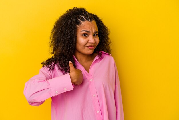 Jeune femme afro-américaine isolée sur un mur jaune surpris en pointant avec le doigt, souriant largement.