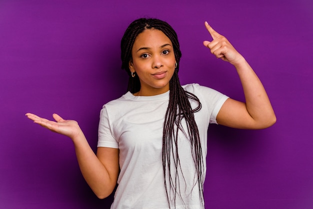 Jeune femme afro-américaine isolée sur mur jaune tenant et montrant un produit en main