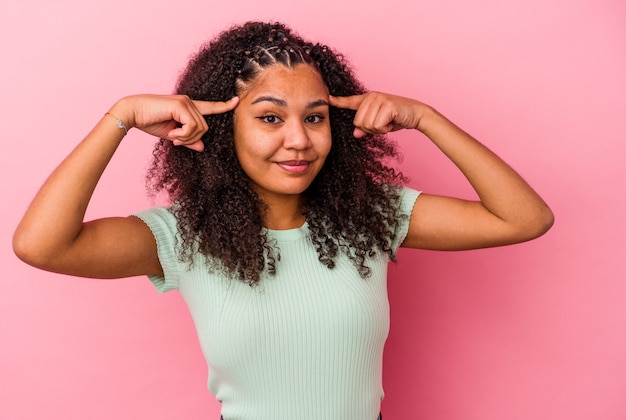 Jeune femme afro-américaine isolée sur un mur rose axé sur une tâche, gardant l'index pointant la tête