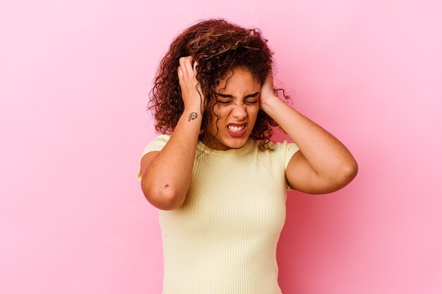 Jeune femme afro-américaine isolée sur un mur rose couvrant les oreilles avec les mains.