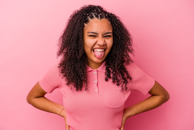 Jeune femme afro-américaine isolée sur le mur rose drôle et sympathique qui sort la langue