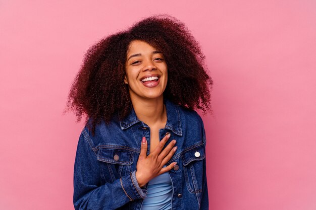 Jeune femme afro-américaine isolée sur le mur rose éclate de rire en gardant la main sur la poitrine.