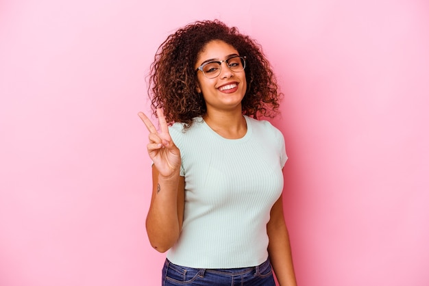 Jeune femme afro-américaine isolée sur le mur rose joyeux et insouciant montrant un symbole de paix avec les doigts.