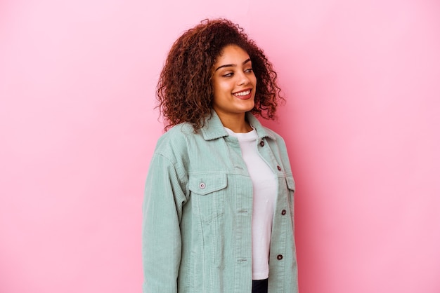 Jeune femme afro-américaine isolée sur le mur rose regarde de côté souriant, joyeux et agréable