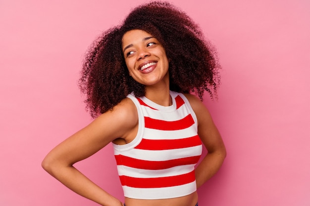 Jeune femme afro-américaine isolée sur le mur rose rit joyeusement et s'amuse à garder les mains sur le ventre.