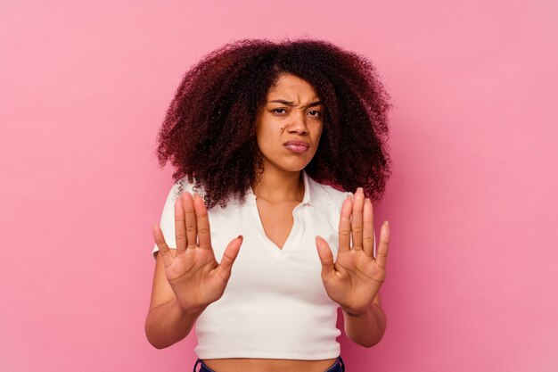 Jeune femme afro-américaine isolée sur rose debout avec la main tendue montrant le panneau d'arrêt, vous empêchant.