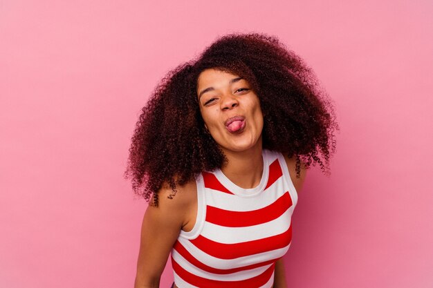 Jeune femme afro-américaine isolée sur rose drôle et sympathique qui sort la langue.