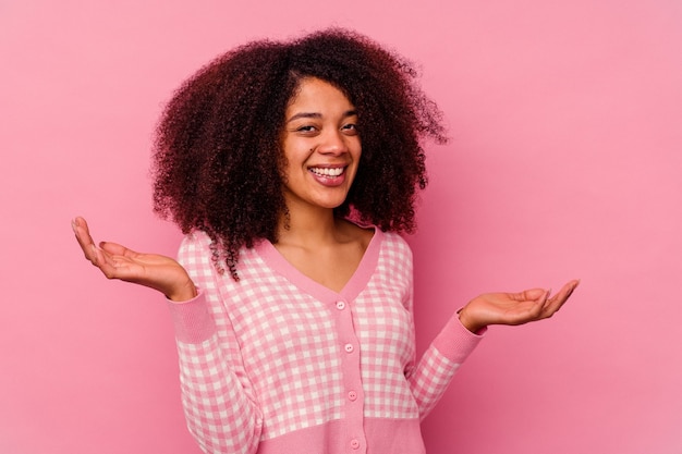 Jeune femme afro-américaine isolée sur rose montrant une expression de bienvenue.