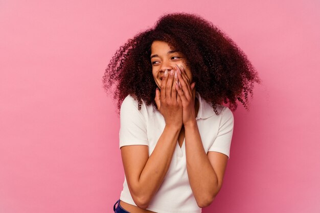 Jeune femme afro-américaine isolée sur rose en riant de quelque chose, couvrant la bouche avec les mains.