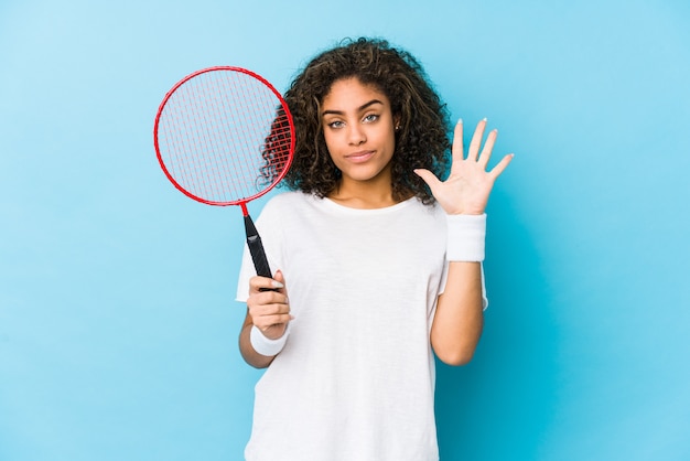 Jeune femme afro-américaine jouant au badminton souriant joyeux montrant le numéro cinq avec les doigts.