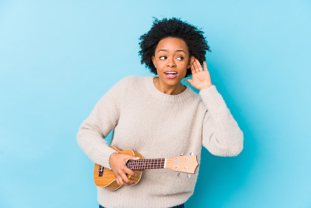 Jeune femme afro-américaine jouant du ukelele isolé essayant d'écouter un commérage.