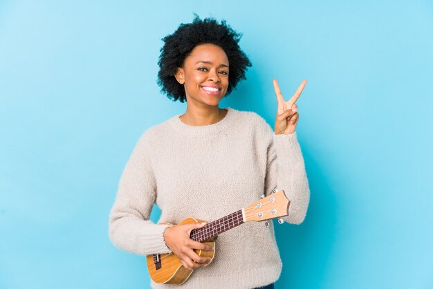 Jeune femme afro-américaine jouant du ukulélé isolé montrant le numéro deux avec les doigts.