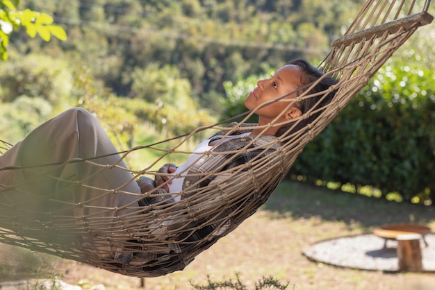 Une jeune femme afro-américaine jouissant de la tranquillité de la nature se balançant doucement et se relaxant dans un