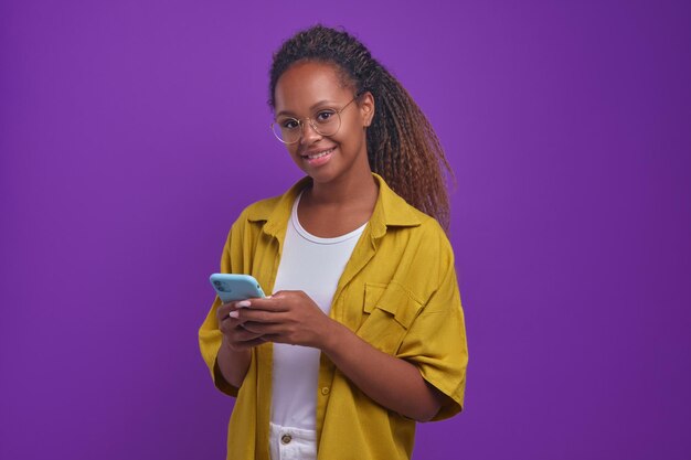 Jeune femme afro-américaine joyeuse à l'aide de supports de téléphone portable en studio