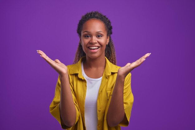 Jeune femme afro-américaine joyeuse lève les mains avec les paumes vers le haut en studio