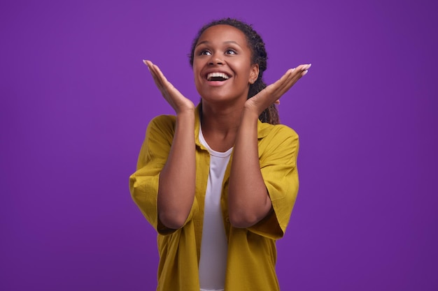 Jeune femme afro-américaine joyeuse lève les yeux avec délice se tient en studio