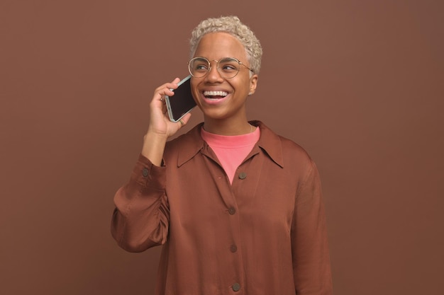 Jeune femme afro-américaine joyeuse rire en faisant un appel au téléphone se tient en studio