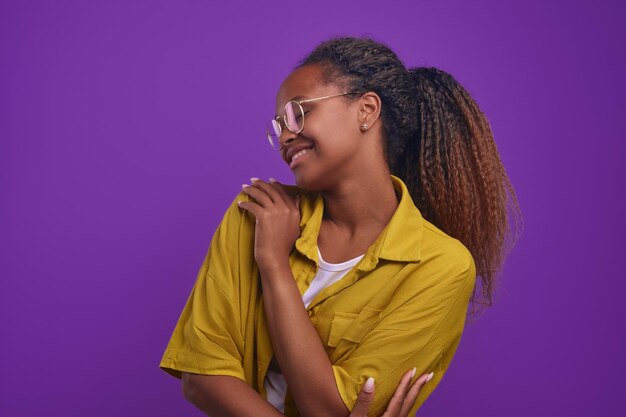 Jeune femme afro-américaine joyeuse se serre dans ses bras et sourit se tient en studio