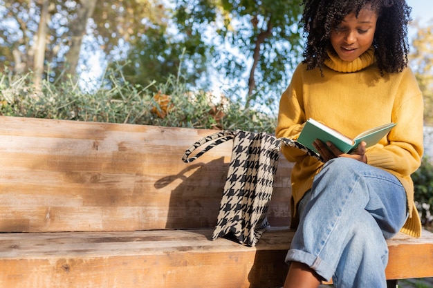 Photo jeune femme afro-américaine lisant un livre assis sur un banc de parc. espace de copie. concept de mode de vie.