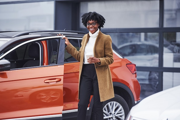 Jeune femme afro-américaine à lunettes se tient à l'extérieur près d'une voiture moderne.