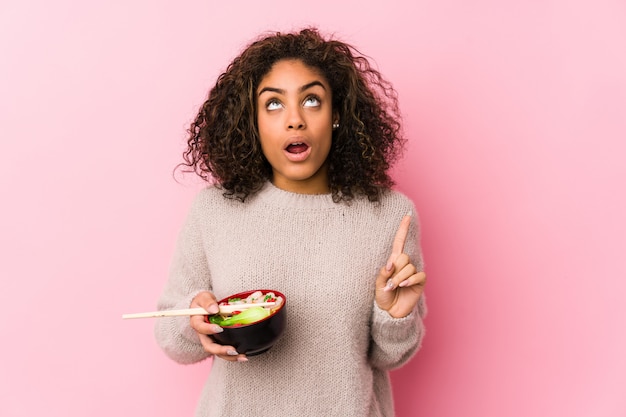 Photo jeune femme afro-américaine, manger des nouilles pointant à l'envers avec la bouche ouverte.