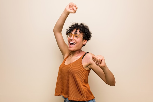 Jeune femme afro-américaine avec la marque de naissance de peau célébrant une journée spéciale, saute et lève les bras avec énergie.