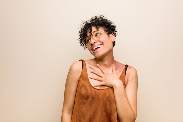 Jeune femme afro-américaine avec la marque de naissance de la peau éclate de rire en gardant la main sur la poitrine.