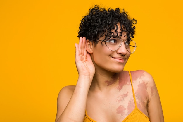 Jeune femme afro-américaine avec la marque de naissance de peau en essayant d'écouter un commérage.