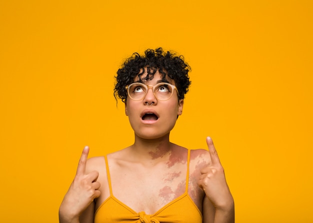 Jeune femme afro-américaine avec la marque de naissance de peau pointant vers le haut avec la bouche ouverte.