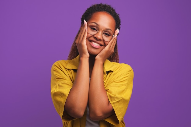 Une jeune femme afro-américaine met les paumes sur les joues et incline la tête en studio