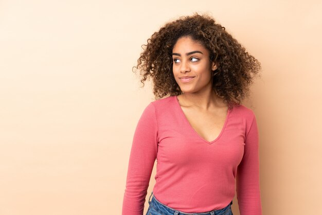 Jeune femme afro-américaine sur mur beige ayant des doutes tout en regardant de côté