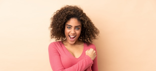 Jeune femme afro-américaine sur mur beige célébrant une victoire